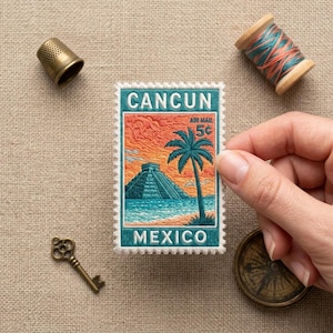 May include: A rectangular embroidered patch featuring a vintage-style postage stamp design with the text CANCUN and MEXICO. The image depicts a Mayan pyramid, a palm tree, and a sunset over the ocean in shades of orange, teal, and blue.