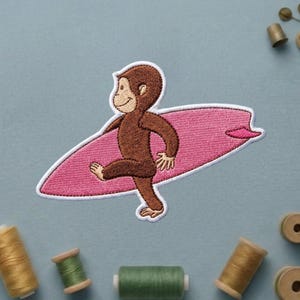 May include: Embroidered patch featuring a brown monkey carrying a pink surfboard with a white border. The monkey is walking with a smile. The patch is likely for clothing or accessories.
