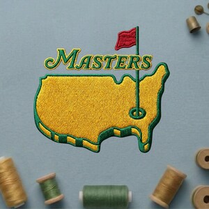 May include: Embroidered patch featuring the word "Masters" in green and gold script above a gold map outline with a green border. A red flag on a green pole is positioned on the map. The patch is on a light blue background with spools of thread.