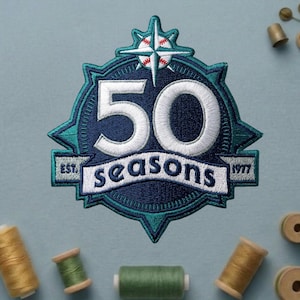 May include: Embroidered patch with a navy blue and teal design. The patch features the number "50" in white, the words "seasons" and "EST. 1977". A baseball-themed compass rose is at the top. The patch is surrounded by spools of thread.