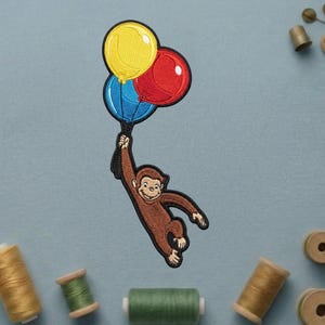May include: Embroidered patch featuring a brown monkey holding three balloons. The balloons are yellow, red, and blue. The patch has a black border and is likely for clothing or accessories.