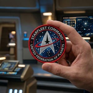 以下が含まれることがあります： Starfleet Command United Federation of Planetsのロゴが入った円形の刺繍ワッペン。青い宇宙の背景に星が散りばめられ、白いデルタのエンブレムと黒い星が描かれています。周囲は赤い縁取りで、白い文字が記されています。