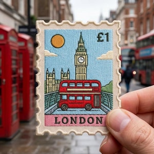 May include: A rectangular embroidered patch shaped like a postage stamp featuring a light blue sky with a yellow sun, the Big Ben clock tower, and a red double-decker bus. The text £1 appears in the top right corner, and the word LONDON is at the bottom.