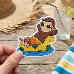 May include: An embroidered patch featuring a brown monkey wearing yellow-rimmed sunglasses, relaxing on a yellow and green polka-dot inflatable pool float. The monkey has orange shorts and is resting with hands behind its head on blue water.