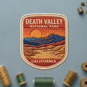 May include: Embroidered patch featuring a Death Valley National Park landscape. The design includes a sunset, mountains, and the text "DEATH VALLEY NATIONAL PARK CALIFORNIA" in a rectangular shape with a cream-colored border.