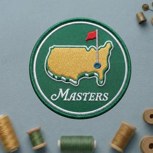 May include: Embroidered patch featuring the Masters Tournament logo. The design includes a green circle with a white border, a yellow map of the United States, a red flag, and the word "Masters" in white script. The patch is surrounded by spools of thread.