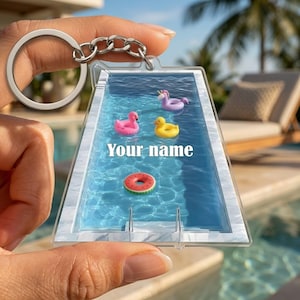 May include: A rectangular acrylic keychain featuring a swimming pool graphic with blue water, a white marble border, and a metal ladder. The pool contains a pink flamingo, a yellow duck, and a watermelon slice float, with the text Your name.