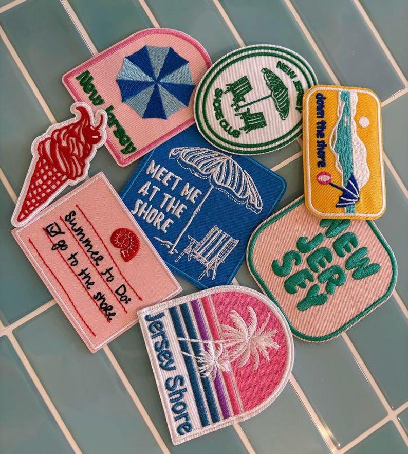 May include: A collection of eight embroidered patches featuring beach-themed designs. The patches include imagery of a red ice cream cone, a blue umbrella, a beach chair, palm trees, and text such as New Jersey, Shore Club, and Summer to Do.