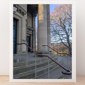 May include: Architectural photograph of a building with large stone columns and steps leading up to the entrance. The image includes a wooden handrail and a tree with bare branches against a blue sky. The words "Digital download" are at the bottom.