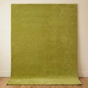 Puede incluir: Una alfombra rectangular de un color verde lima sólido y vibrante. La alfombra presenta una textura densa de pelo corto con una apariencia uniforme en toda su superficie, mostrada verticalmente contra una pared lisa.