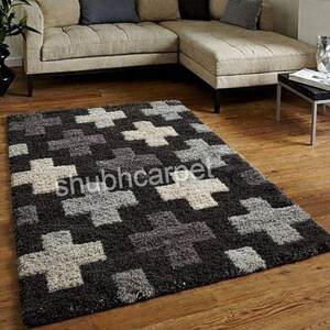 Può includere: Un tappeto rettangolare con un motivo a croce ripetuto in tonalità di nero, grigio e beige. Il tappeto è posato su un pavimento in legno. Il testo "shubhcarpet" è visibile sul tappeto.