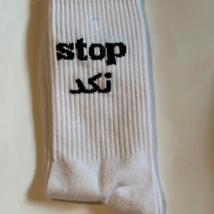 May include: White ribbed socks with the word "stop" and Arabic text printed in black. The socks are folded and appear to be made of a soft, breathable material.