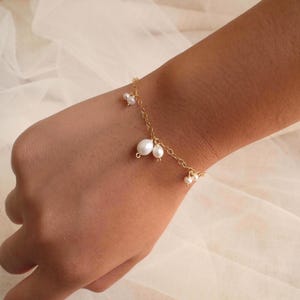 May include: A delicate gold chain bracelet featuring several small, white, irregularly shaped freshwater pearls dangling at intervals along the length of the chain. The bracelet is secured around the wrist with a simple, thin metal link design.