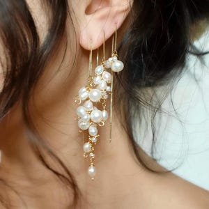 May include: A gold chain threader earring featuring a cluster of white freshwater pearls of varying sizes. The pearls are attached to delicate gold chains that hang from the earlobe, creating a cascading, multi-layered effect with a metallic finish.
