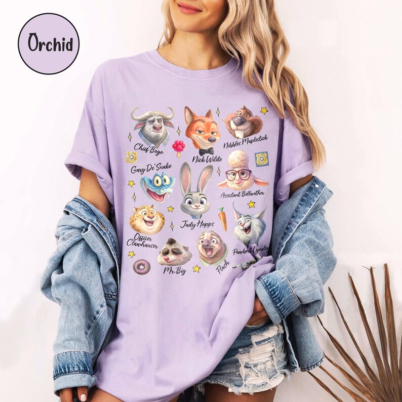 K&ouml;nnte beinhalten: Ein helllila T-Shirt mit Illustrationen von Zeichentrickfiguren. Das Shirt enth&auml;lt den Text "Orchid" in einem Kreis. Die Illustrationen zeigen einen B&uuml;ffel, einen Fuchs, ein Kaninchen und andere Charaktere.
