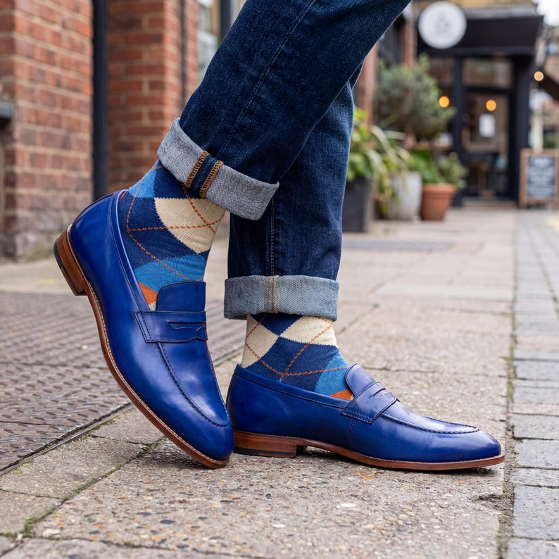 Detailed side view of blue leather penny loafers paired with blue and tan argyle socks and cuffed jeans.