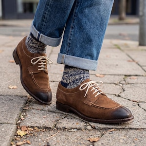 Peut inclure: Chaussures en cuir suédé marron avec lacets blancs et bout foncé. Elles sont associées à un jean bleu et des chaussettes à motifs. Ces chaussures au design classique conviennent à diverses occasions.