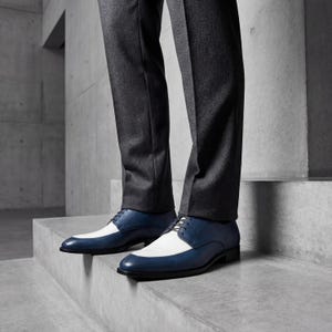 Man wearing blue and white spectator shoes with dark denim jeans and blue argyle socks.