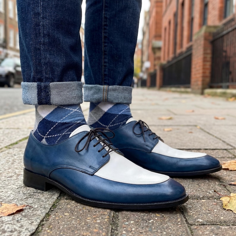 Man wearing blue and white spectator shoes with dark denim jeans and blue argyle socks.