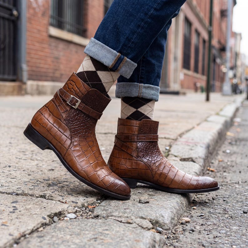 Fashionable man wearing brown crocodile boots and argyle socks on a textured city sidewalk.