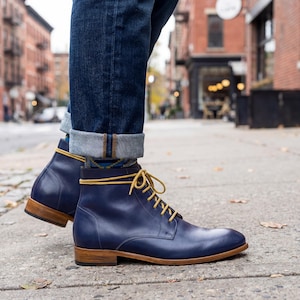 Navy blue leather boots with contrast yellow laces walking on a city sidewalk.