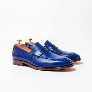 Studio shot of premium blue leather loafers featuring wooden shoe trees against a clean white background.