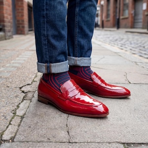 Top-down view of polished red leather penny loafers on a city sidewalk highlighting the almond toe shape.