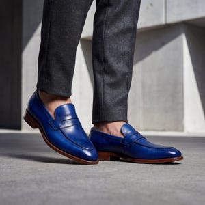 Man walking in handmade blue leather dress shoes with grey wool trousers on a concrete outdoor walkway.