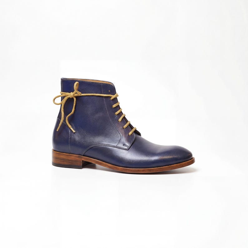 Hand-dyed navy leather mens boot with mustard yellow laces against a white background.