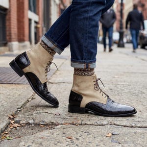 Puede incluir: Botas con cordones de cuero color canela y negro con un patrón texturizado similar al de un cocodrilo en la puntera y el talón. Las botas tienen una parte superior de color canela similar al ante. Las botas se combinan con calcetines estampados y vaqueros azules.