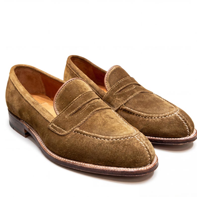 Detail shot of the penny loafer strap and high-quality suede texture on a white background.