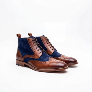 Side view of men's two-tone wingtip boots in brown leather and navy blue suede on white background.
