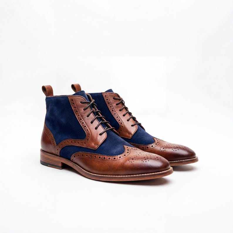 Side view of men's two-tone wingtip boots in brown leather and navy blue suede on white background.