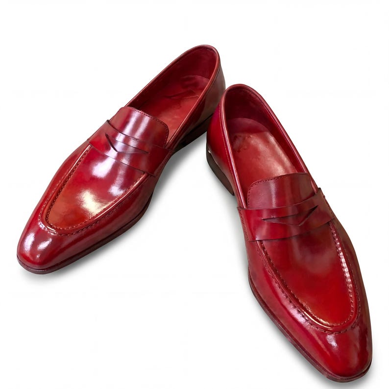 Studio shot of cherry red leather loafers against a white background showing the hand-stitched apron detail.