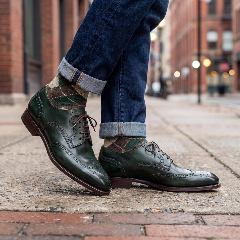 Emerald green wingtip shoes paired with navy argyle socks and cuffed denim jeans.
