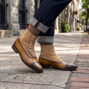 Victorian style mens boots with functional button closure and red pull tab shown on city sidewalk with denim.