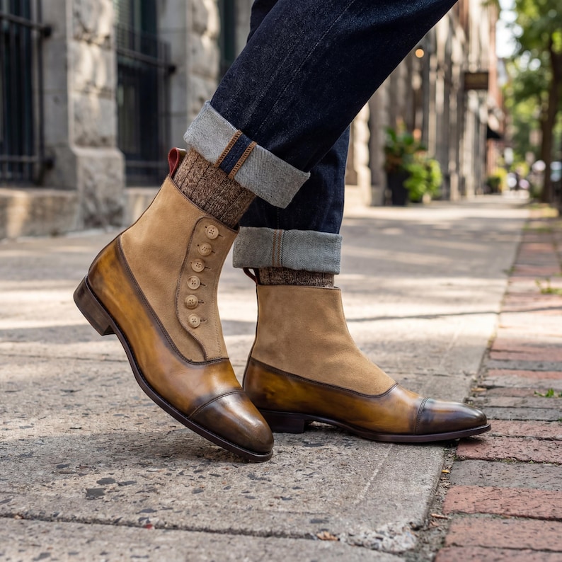 Victorian style mens boots with functional button closure and red pull tab shown on city sidewalk with denim.