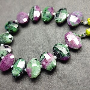 Puede incluir: Un collar de cuentas facetadas de rubí zoisita. Las cuentas ovaladas muestran una mezcla de tonos rosa intenso y verde. Cada cuenta mide aproximadamente 1 cm de largo. Las cuentas están ensartadas con hilo blanco, para un collar o pulsera.