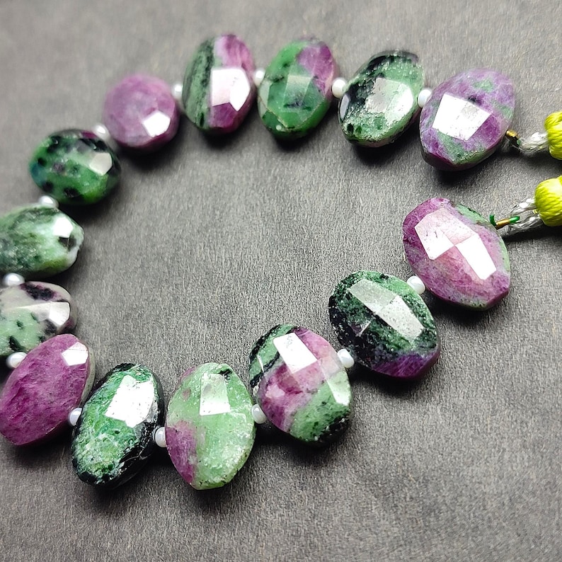 Puede incluir: Un collar de cuentas facetadas de rub&iacute; zoisita. Las cuentas ovaladas muestran una mezcla de tonos rosa intenso y verde. Cada cuenta mide aproximadamente 1 cm de largo. Las cuentas est&aacute;n ensartadas con hilo blanco, para un collar o pulsera.