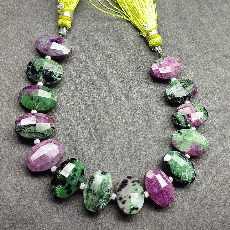 Puede incluir: Un collar de piedras preciosas ovales facetadas en tonos verdes y magenta. Las piedras preciosas est&aacute;n ensartadas con peque&ntilde;as cuentas blancas. El collar est&aacute; rematado con una borla verde lima.