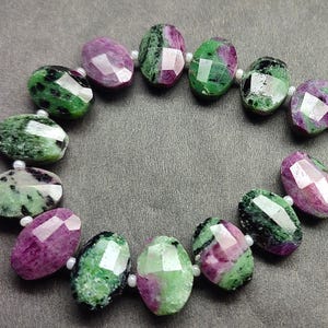 Puede incluir: Un collar de cuentas de piedras preciosas facetadas. Las cuentas ovaladas muestran una mezcla de tonos verdes y rosa intenso. Cada cuenta est&aacute; separada por una peque&ntilde;a cuenta blanca. Las piedras preciosas est&aacute;n dispuestas en c&iacute;rculo.