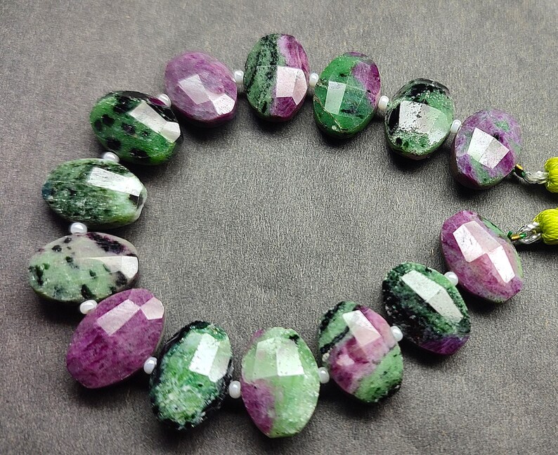 Puede incluir: Un collar de cuentas de piedras preciosas facetadas. Las cuentas ovaladas muestran una mezcla de tonos verdes y rosa intenso. Cada cuenta est&aacute; separada por una peque&ntilde;a cuenta blanca. Las piedras preciosas est&aacute;n dispuestas en c&iacute;rculo.