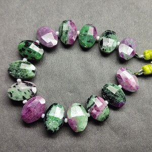 Puede incluir: Un collar de cuentas de piedras preciosas facetadas. Las cuentas de forma ovalada son una mezcla de verde y morado. Las cuentas est&aacute;n ensartadas con peque&ntilde;as cuentas blancas y un cord&oacute;n amarillo y verde.