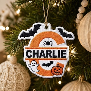 May include: A white and orange embroidered ornament shaped like the letter C, featuring black bats, a spider, a white ghost, and an orange pumpkin. The name CHARLIE is stitched in black letters across the center of the letter C, suspended by a gold cord.