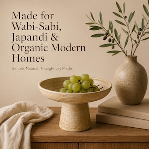 May include: A beige ceramic pedestal bowl filled with green grapes, a small vase with olive branches, and a folded beige cloth on a wooden surface. Text reads "Made for Wabi-Sabi, Japandi & Organic Modern Homes."