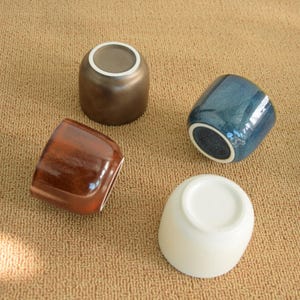 Può includere: Una tazza di ceramica bianca con manico nero e la scritta "But First, Coffee" in nero, con un carattere a mano. La tazza è su una superficie bianca.