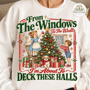 May include: A white sweatshirt featuring a graphic of two children decorating a Christmas tree with a puppy, surrounded by presents. The text reads, From The Windows To The Walls I'm About To DECK THESE HALLS, in green and red lettering.