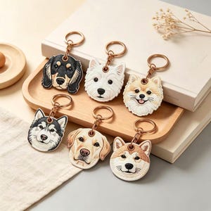 Könnte beinhalten: Sechs bestickte Schlüsselanhänger in Hundeform mit goldfarbenen Metallringen. Die Motive zeigen einen schwarz-lohfarbenen Dackel, einen weißen West Highland Terrier, einen beigen Zwergspitz, einen schwarz-weißen Husky, einen gelben Labrador und einen beigen Shiba Inu.