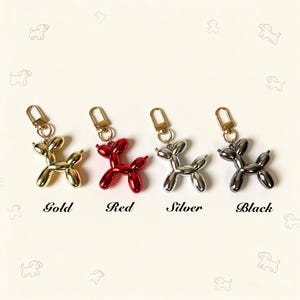 May include: Four balloon dog keychains with metallic finishes in gold, red, silver, and black. Each keychain features a lobster clasp and a smooth, reflective surface shaped like a twisted balloon animal. The words Gold, Red, Silver, and Black are printed below each corresponding keychain.