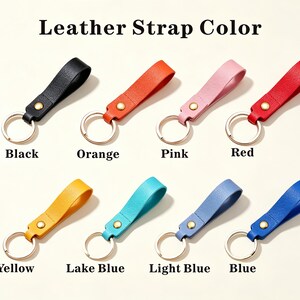 May include: Eight leather keychains arranged in two rows with the text Leather Strap Color above. Each keychain features a textured leather loop in black, orange, pink, red, yellow, lake blue, light blue, or blue, secured by a gold rivet and ring.